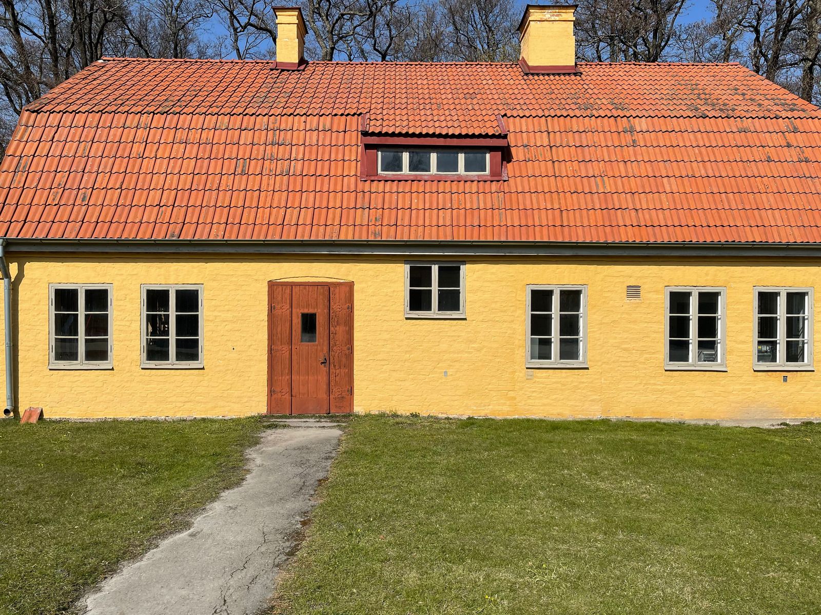 Ældre gulkalket hus med rødt tegltag, kvist og græsplæne foran