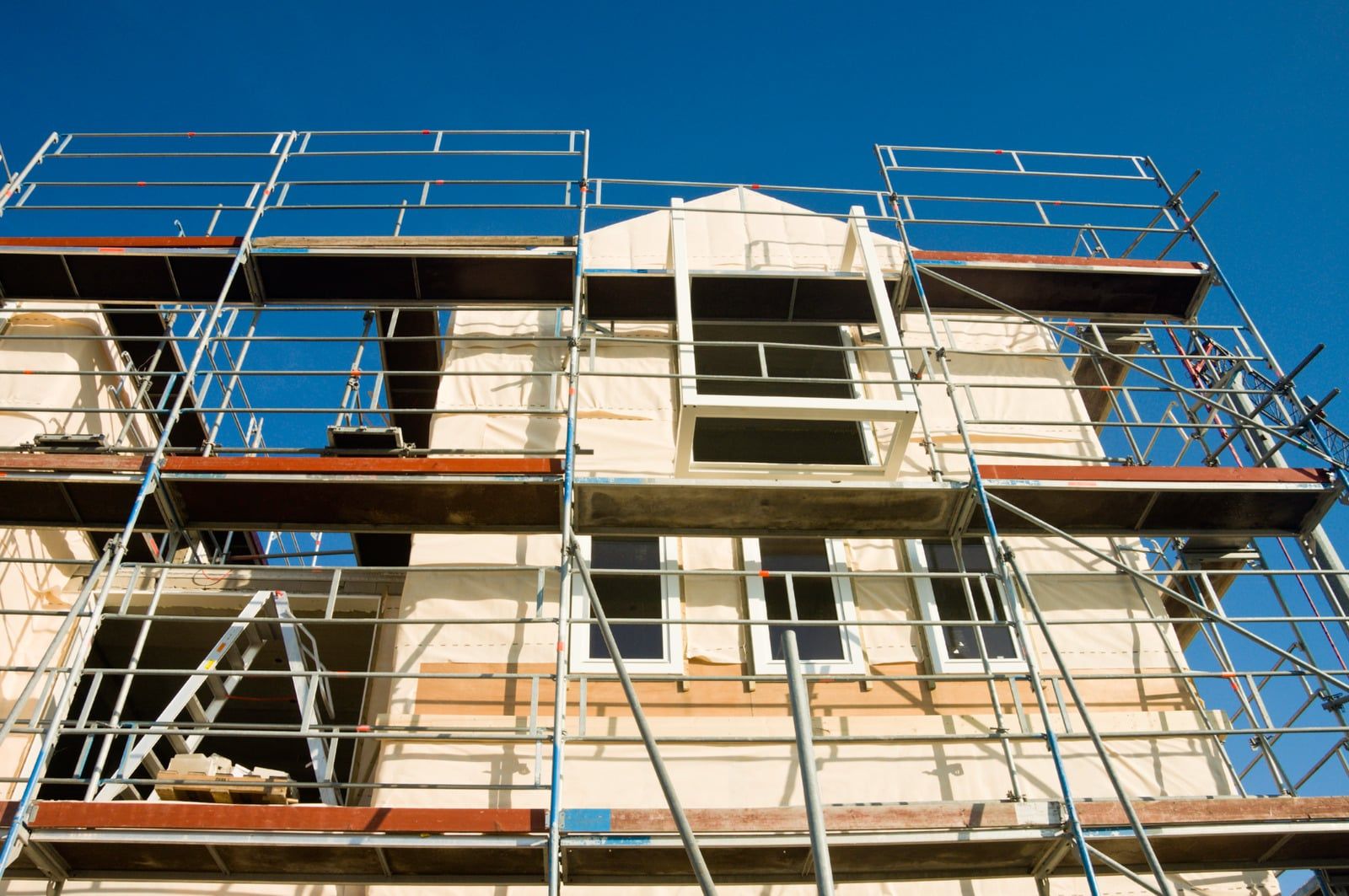 Hus med stillads hele vejen rundt og ny facadeisolering under renovering mod en blå himmel