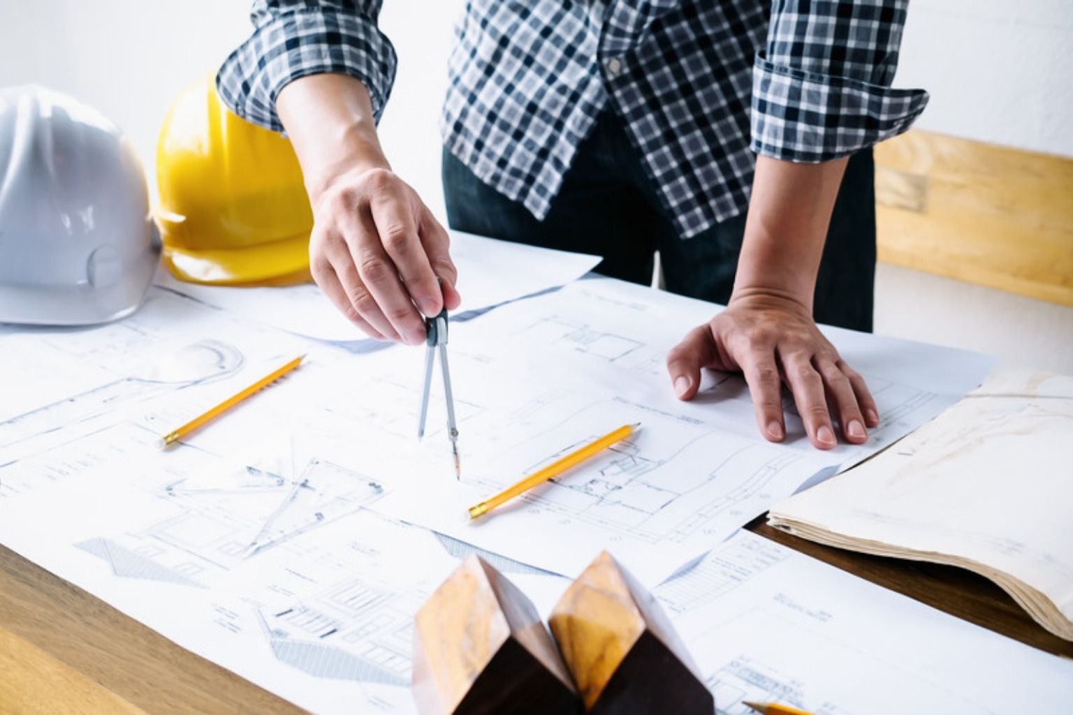 Byggeleder arbejder med passer på tegninger ved siden af sikkerhedshjelme