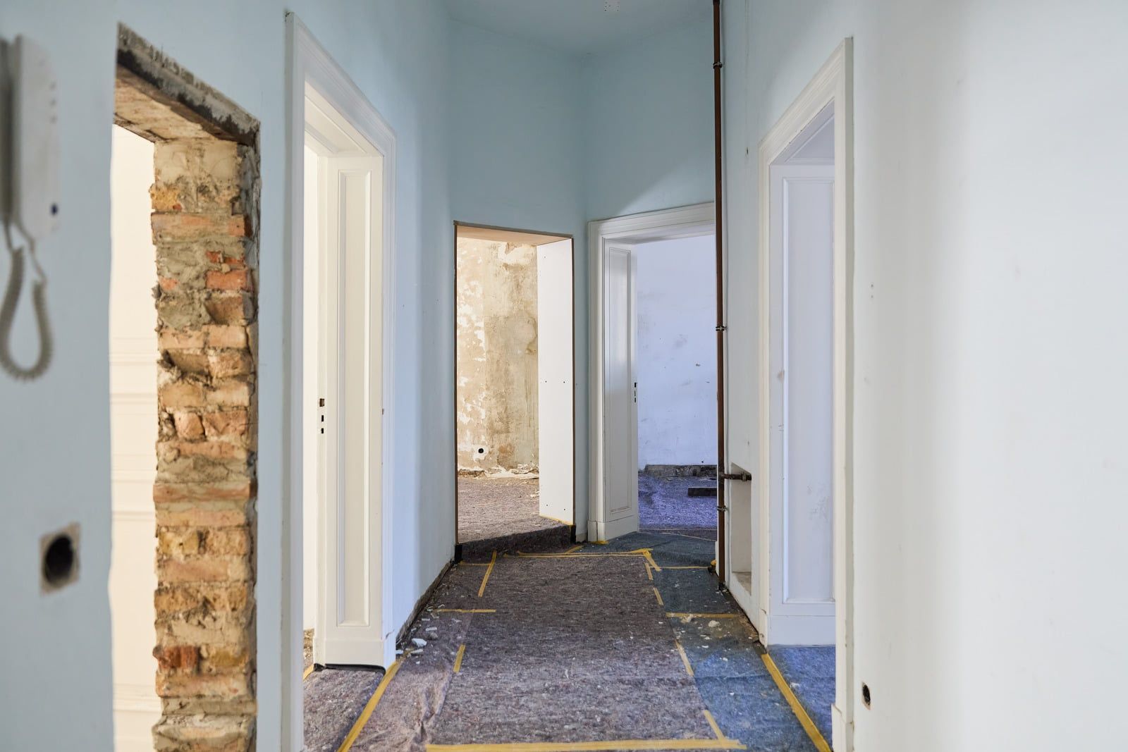 Gang i en lejlighed under renovering med afdækket gulv, nye dørkarme og en blottet murstensåbning