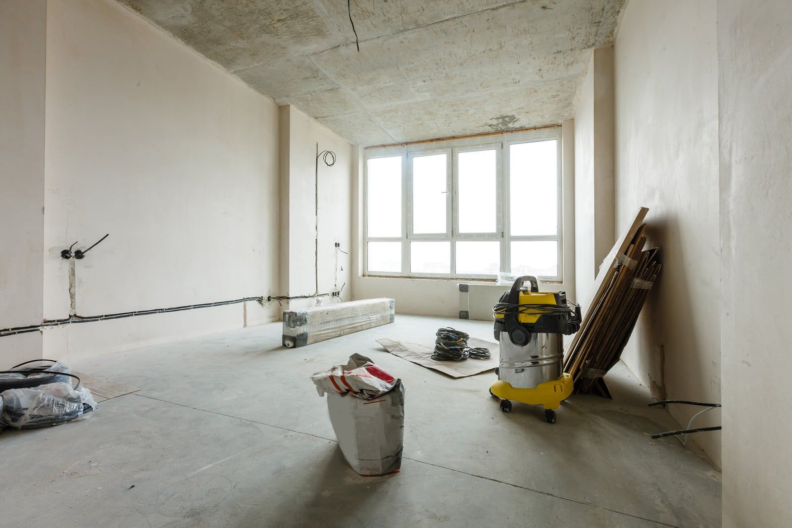 Lyst, tomt rum under renovering med spartlede vægge, støvsuger og materialer på betongulvet